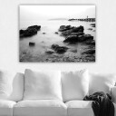 Lerretsbilde 70x100 cm Fredelig kystlandskap med klipper og en brygge i det fjerne Svart / Hvit / Grå